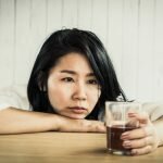 Woman with a chronic drinking issue and cardiomyopathy staring at glass of liquor